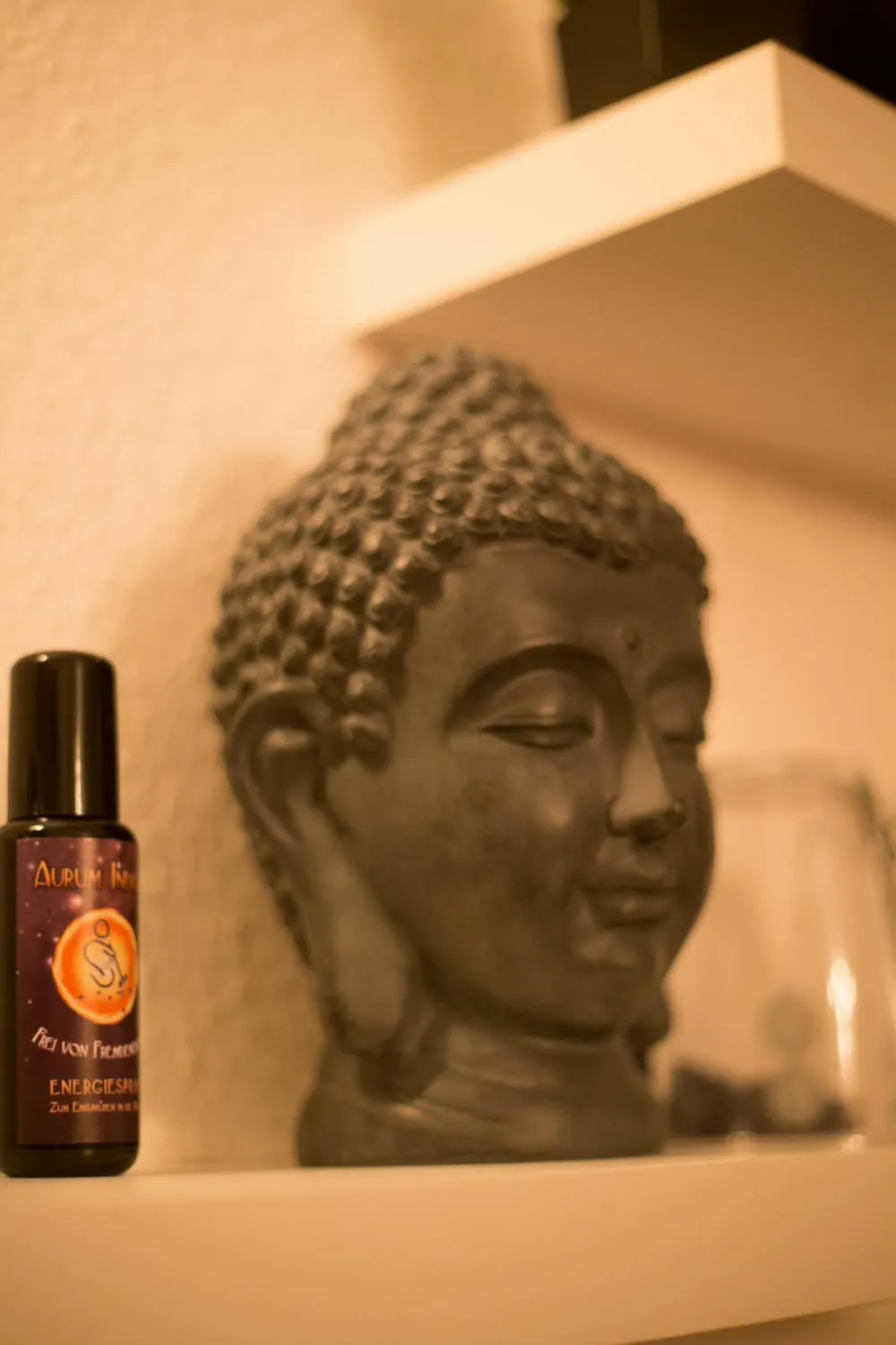 Ein Buddhakopf aus Stein und ein Fläschchen Energiespray auf einem Wandregal in Christianes Raum.