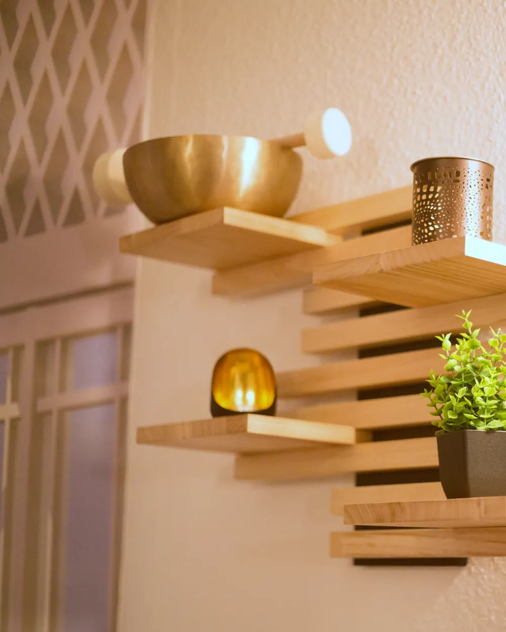 Eine goldene Klangschale, ein Windlicht und eine Pflanze auf Holzregalen in Christianes Raum.